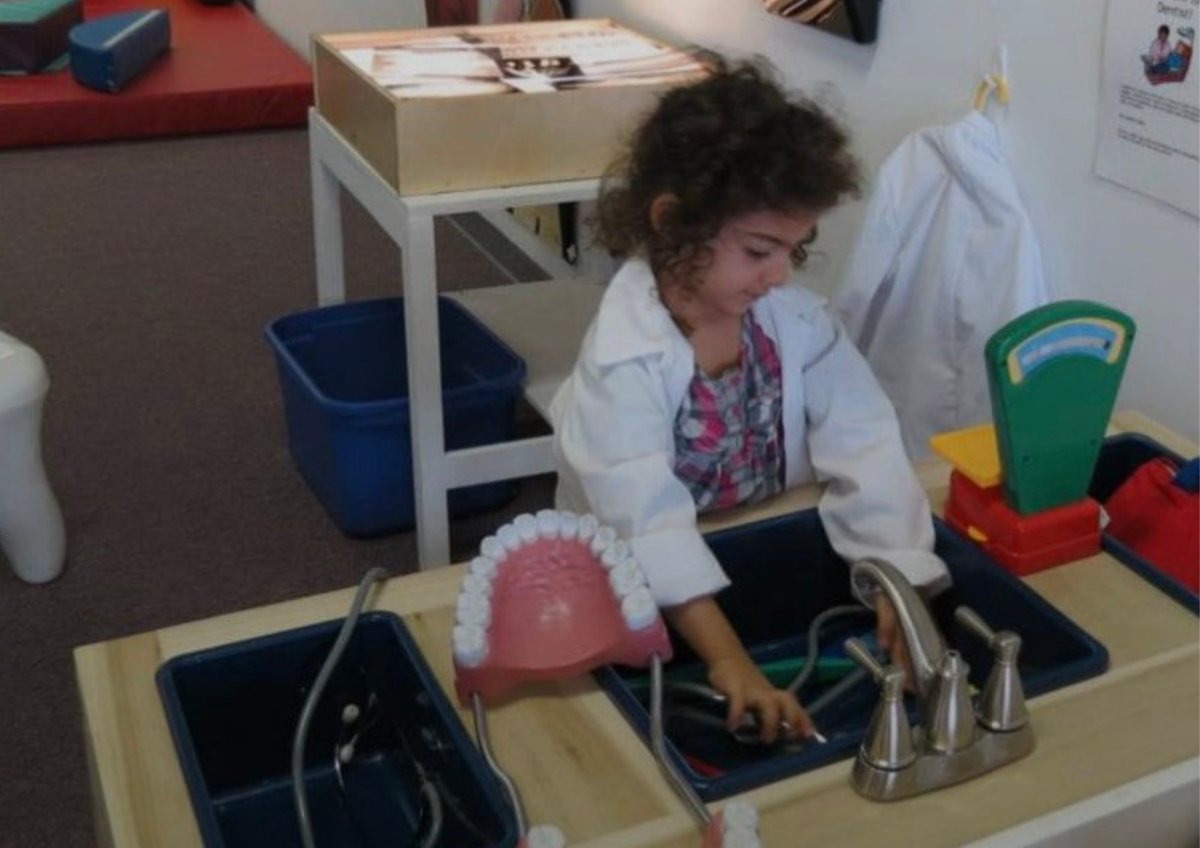 A young Tara in a white lab coat, exploring a hands-on science station as a child.